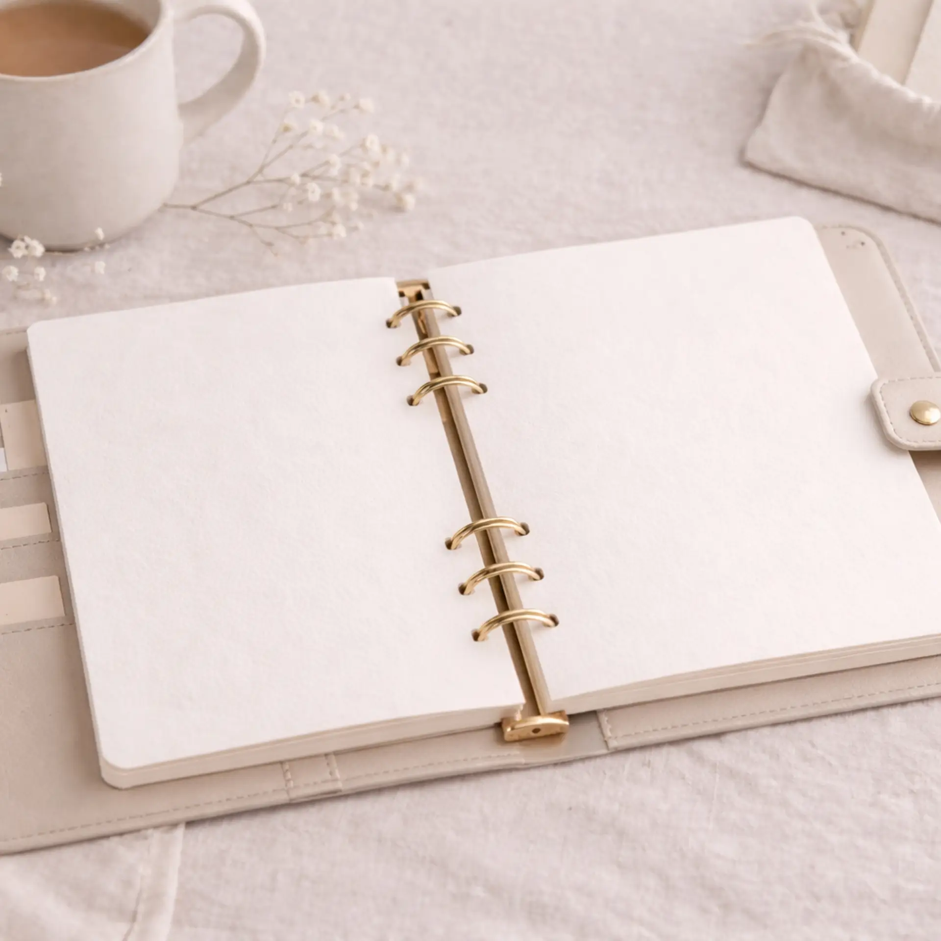 no text. decorative 6 ring leather planner with neutral background, coffee mug, scripture focus card pouch, and baby breath plant.